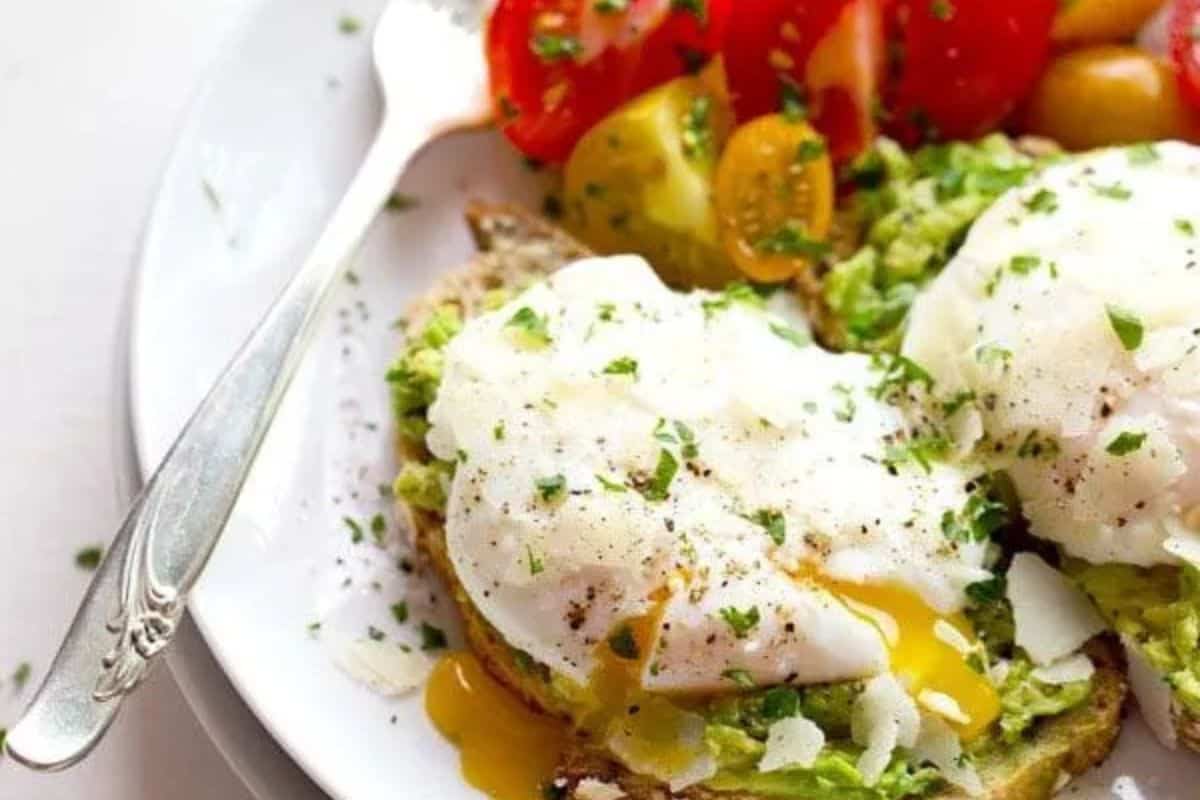 A plate with avocado toast topped with poached eggs, served with sliced cherry tomatoes and garnished with chopped herbs—one of the easy Weight Watchers recipes perfect for a healthy and delicious start to your day.