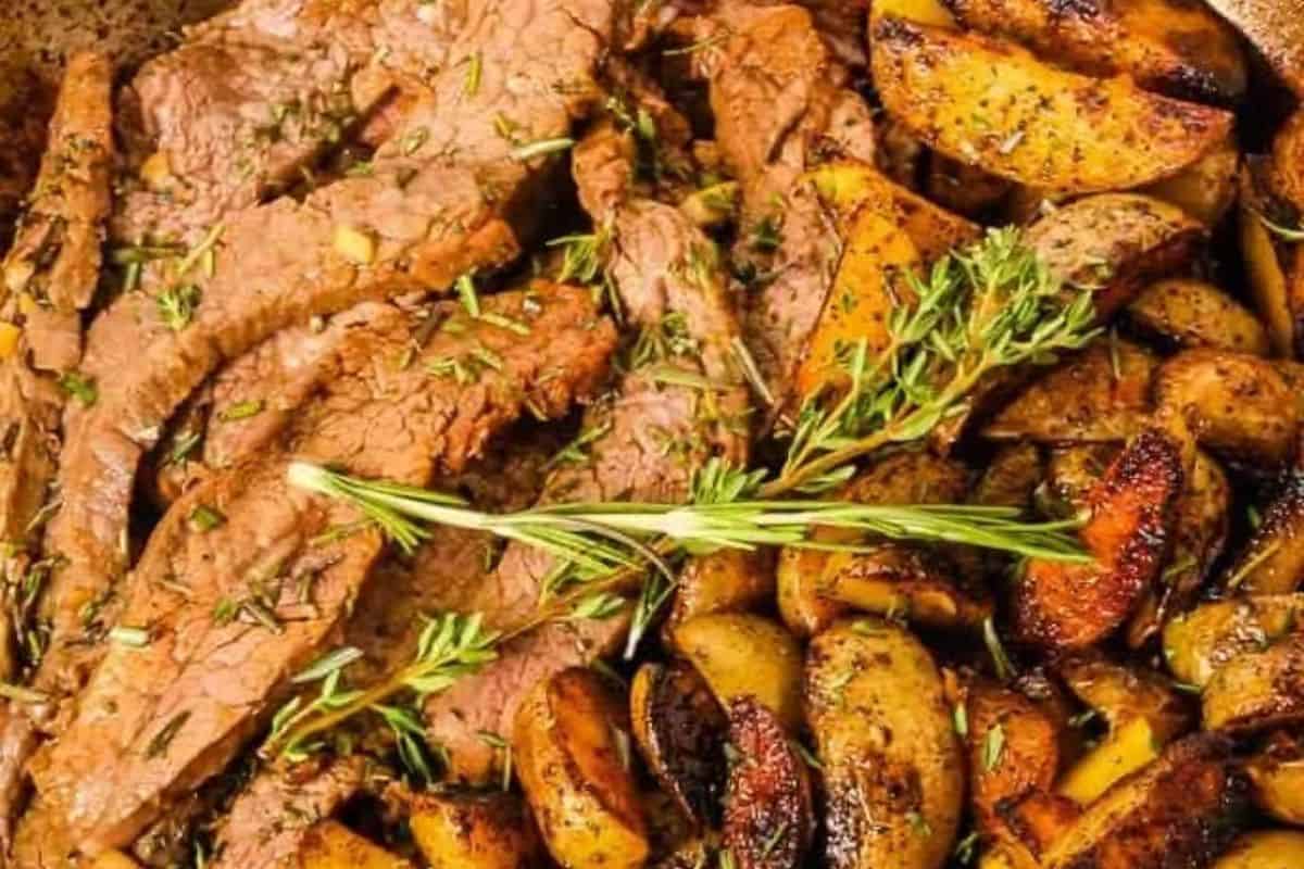 Close-up of sliced flank steak with roasted potato wedges, garnished with rosemary and thyme.