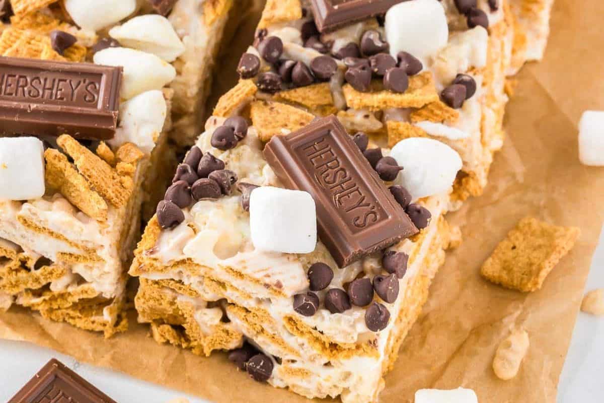 Irresistible s'mores rice krispie treat topped with marshmallows, chocolate chips, and small Hershey's chocolate pieces elevate your snack game on parchment paper.