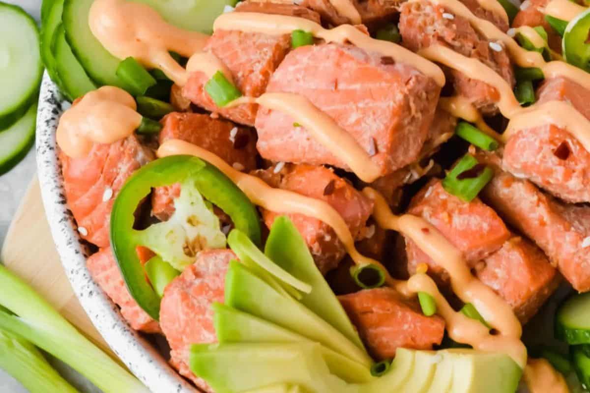A bowl of diced salmon topped with spicy sauce, sliced avocado, cucumbers, jalapeños, green onions, and sesame seeds is an irresistible salmon creation everyone will love.