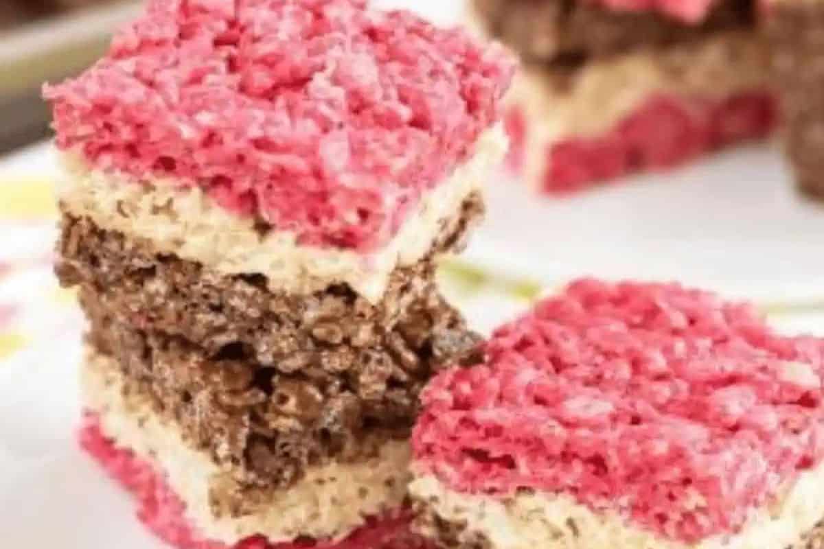 Stacked on a plate, these irresistible strawberry chocolate rice crispy treats feature delightful pink, chocolate, and plain layers. Perfect for elevating your snack game with a burst of color and flavor!.
