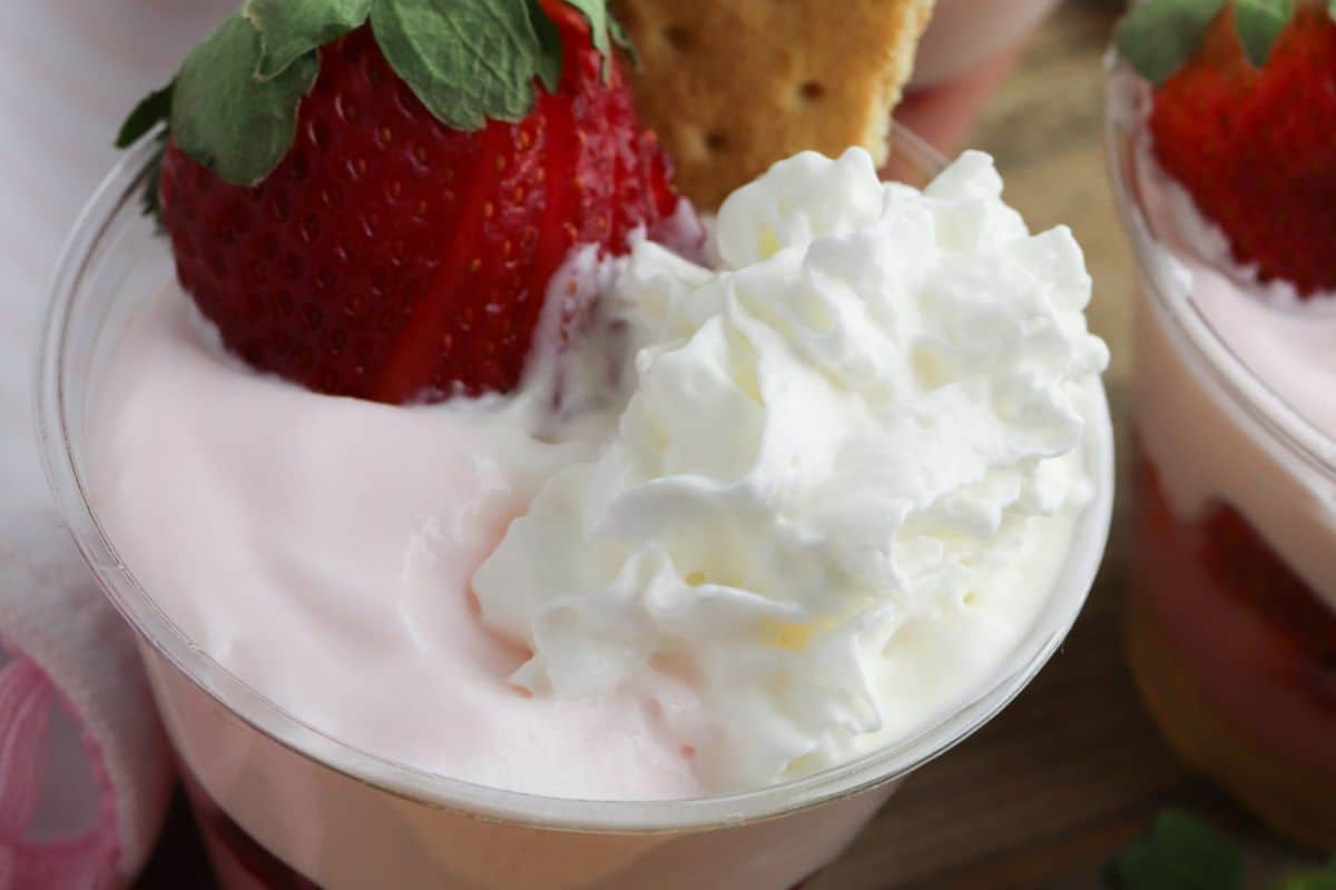A delightful strawberry pudding parfait featuring a creamy mixture topped with whipped cream, a biscuit, and a whole strawberry, perfect for indulging with your bestie or adding to your festive recipes collection for Galentine’s Day.