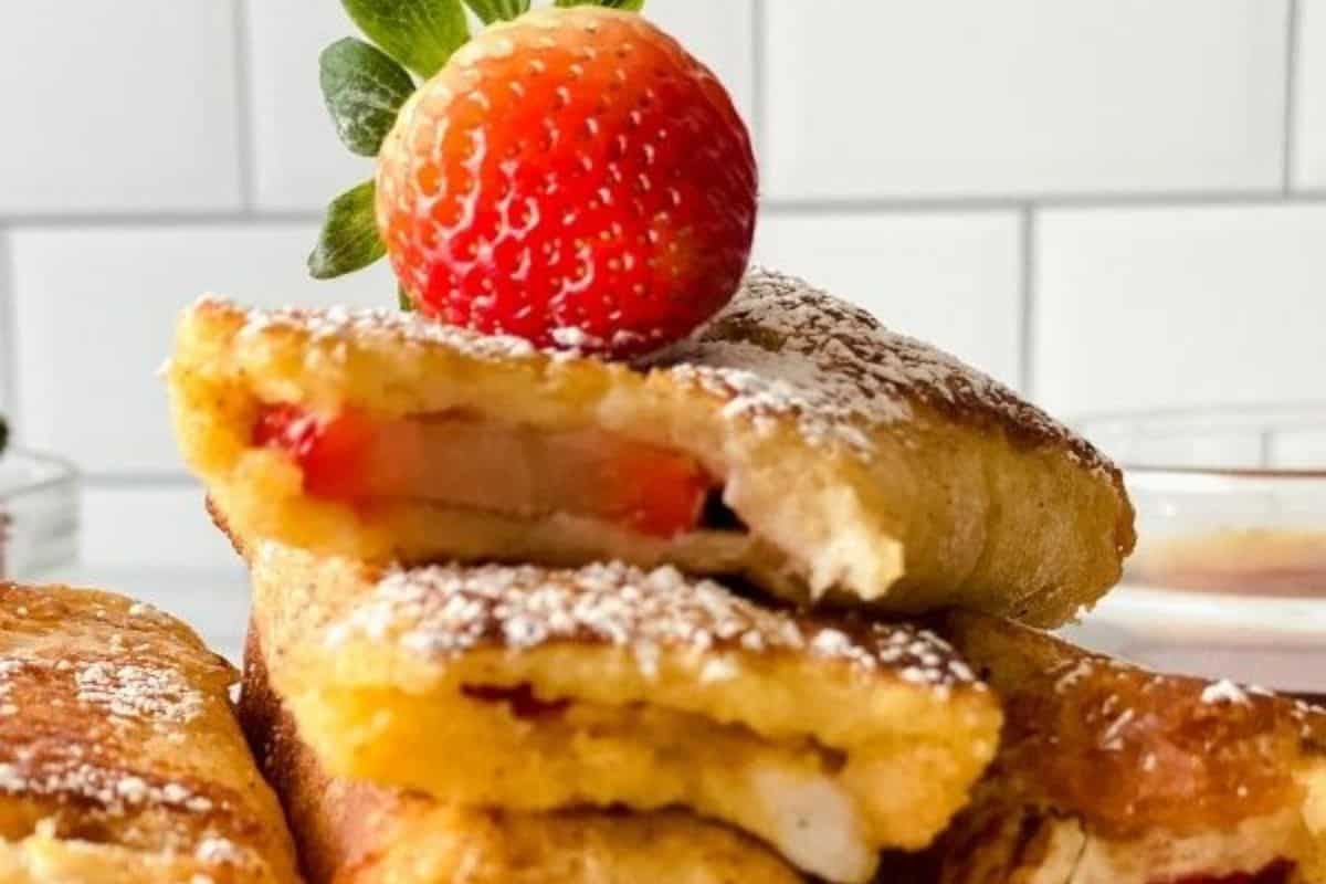 Close-up of strawberry stuffed French toast rolls, perfect for a delightful brunch, lightly dusted with powdered sugar on a tiled background.