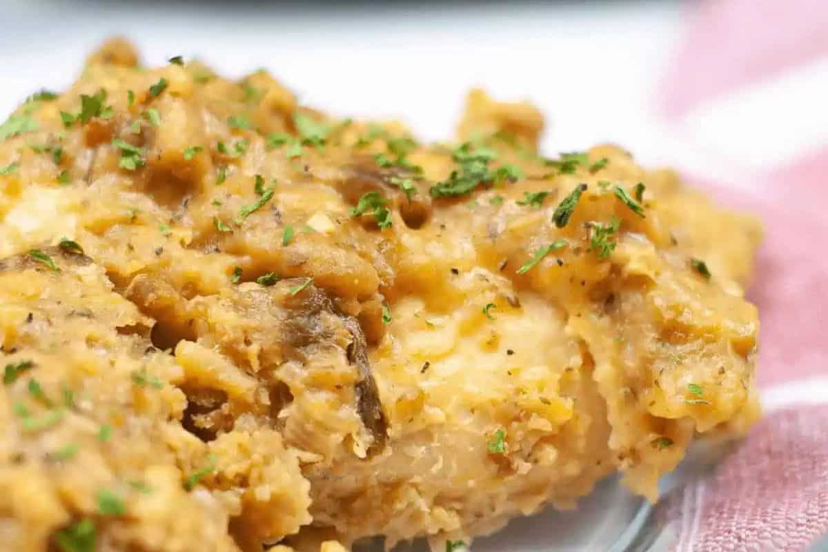 A close-up of a baked chicken breast covered in a creamy, golden-brown sauce and garnished with chopped herbs—perfect for elevating your dinner routine.