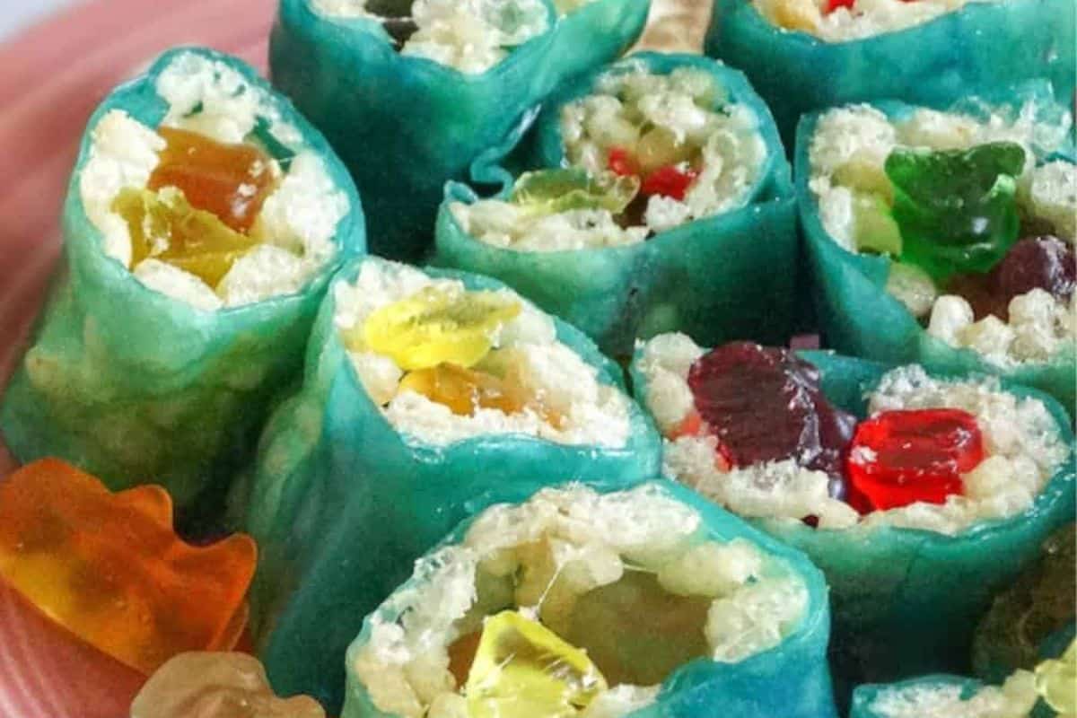 Indulge in an irresistible rice krispie treat featuring colorful candy sushi rolls. Wrapped in blue rice paper with gummy bears and a Rice Krispie filling, these creations elevate your snack game. Served on a vibrant pink plate, they're a playful twist on classic Rice Krispie Treat recipes.