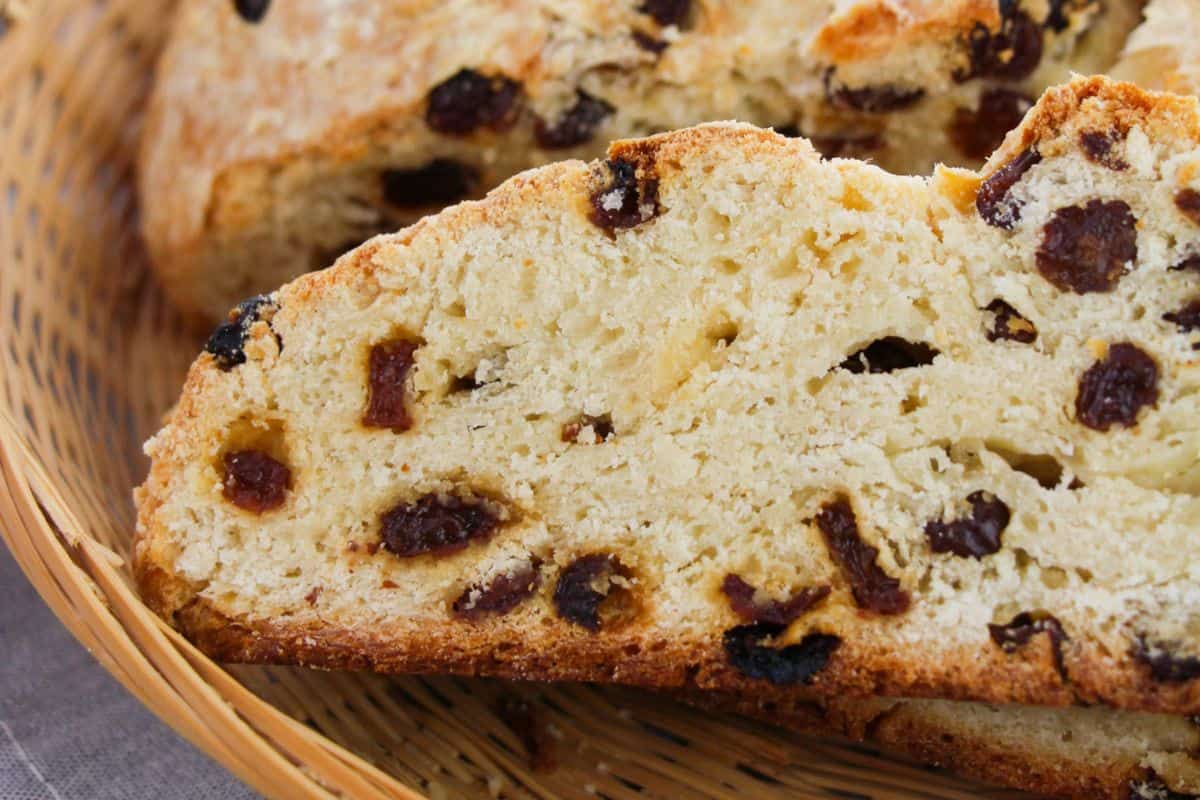 Close-up of crowd-pleasing sliced Irish soda bread with raisins nestled in a woven basket, perfect for potluck recipes.