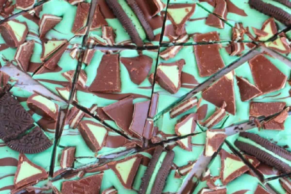 A cute close-up of fractured mint chocolate bark showcases layers of chocolate and mint cream, with Oreo pieces sprinkled throughout. The festive treat is perfect for St. Patrick’s Day celebrations or any day you crave a touch of sweetness.