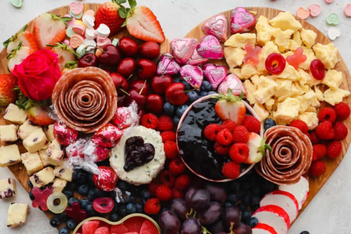 A heart-shaped charcuterie board perfect for Galentine’s Day, featuring assorted fruits, cheeses, salami roses, chocolates, and scrambled eggs. Garnished with berries and candies, it's a festive recipe that adds a delightful touch to any celebration.