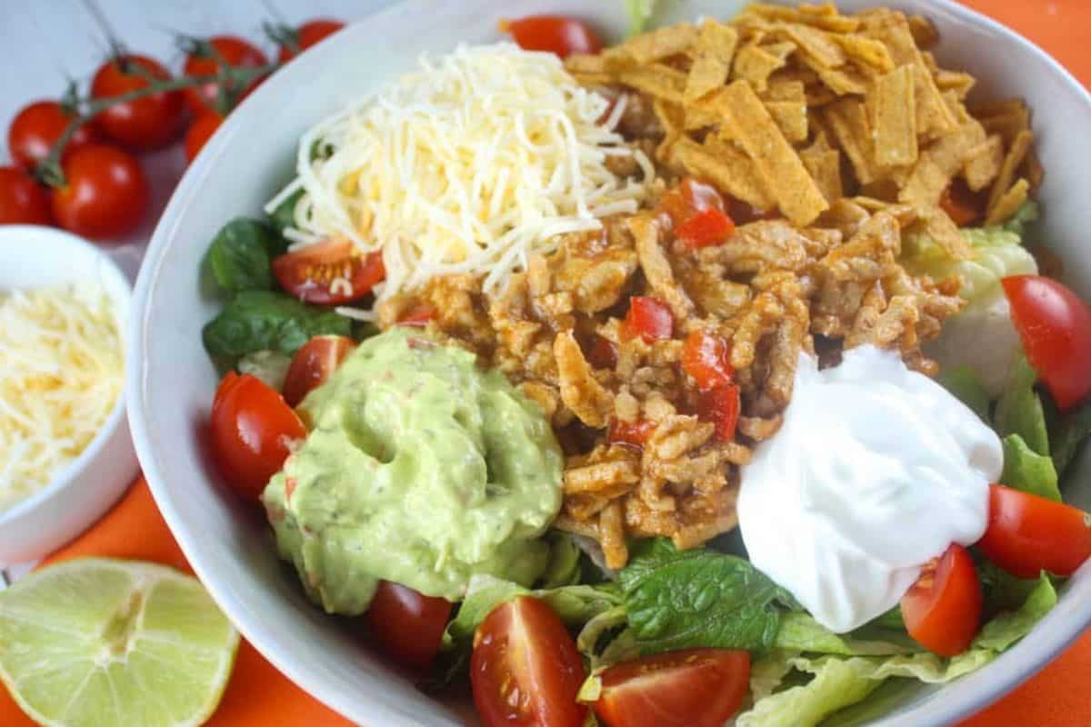 A taco salad with shredded cheese, tortilla strips, seasoned ground meat, guacamole, sour cream, and chopped tomatoes on lettuce—perfect for those seeking Easy Weight Watchers Recipes.
