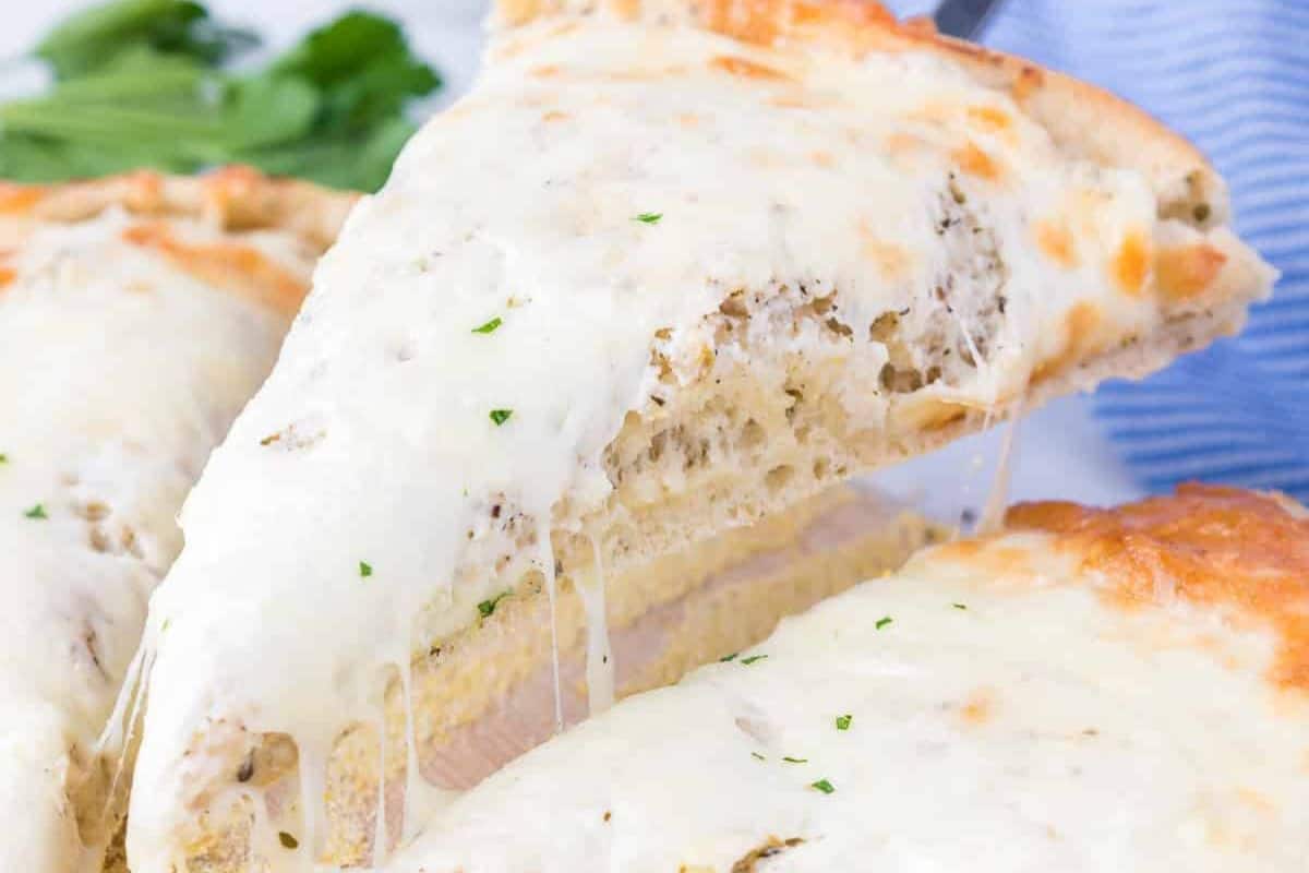 Close-up of a white pizza slice being lifted, with melted cheese stretching from the rest of the pizza. In the background, a hint of greenery and a cozy cloth suggests this scene is part of the perfect night in, inspired by our favorite pizza recipes.