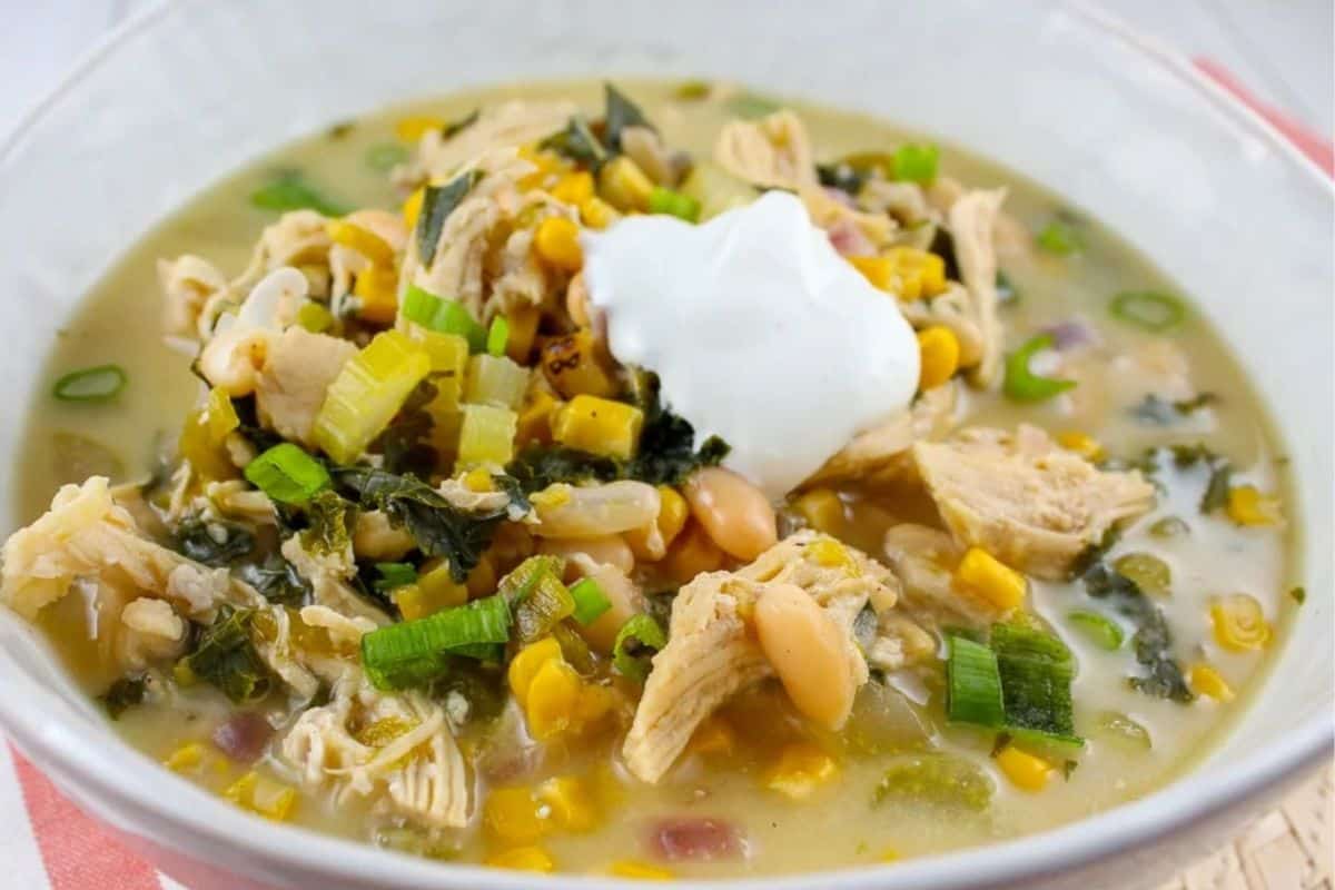 A bowl of white chicken chili with shredded chicken, corn, beans, chopped green onions, and a dollop of sour cream on top—perfect for anyone looking for easy Weight Watchers recipes.