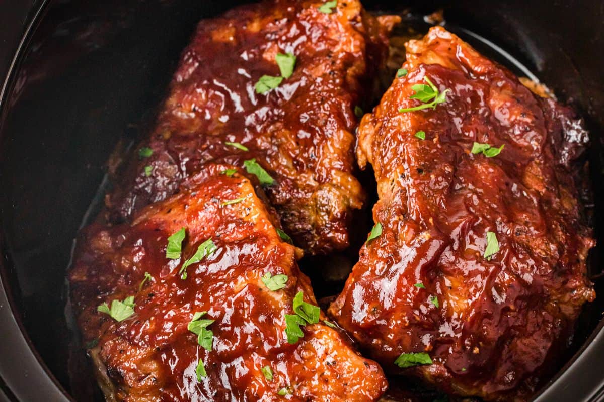Three pieces of barbecued ribs coated in sauce and garnished with chopped parsley in a black dish—perfect for easy dinner nights or as inspiration for your favorite slow cooker recipes.