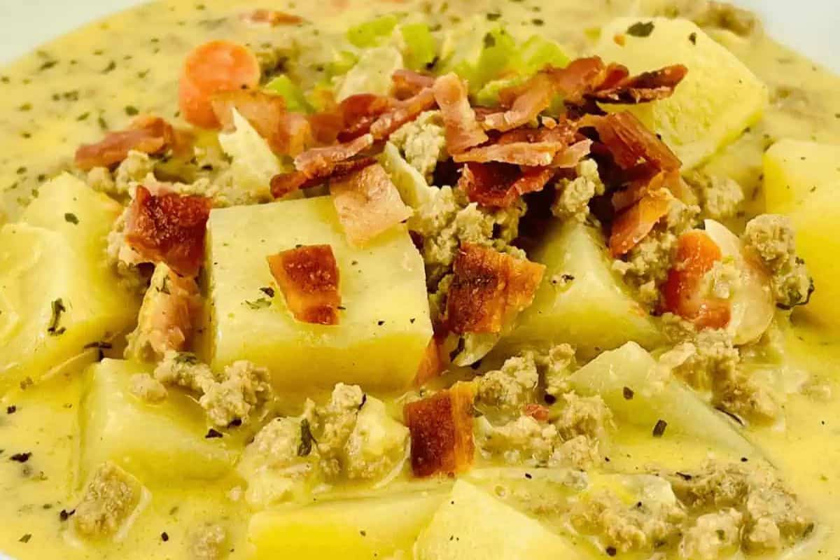 A close-up of a creamy, comforting soup containing diced potatoes, ground meat, carrots, and topped with crispy bacon pieces—perfect for those seeking quick soups ready in just 30 minutes.