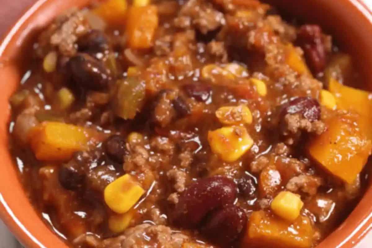 Close-up of a bowl of chili containing ground meat, kidney beans, corn, diced tomatoes, and chunks of vegetables in a thick sauce—a must try for fans of classic chili recipes.