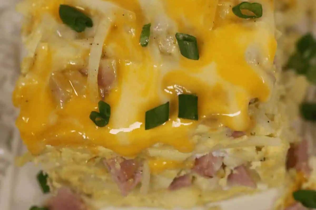 Close-up of a cheesy breakfast casserole topped with melted cheddar and green onions, showing layers of ham and shredded potatoes—a sweet and savory dish perfect for Valentine's Day breakfast or brunch recipes.