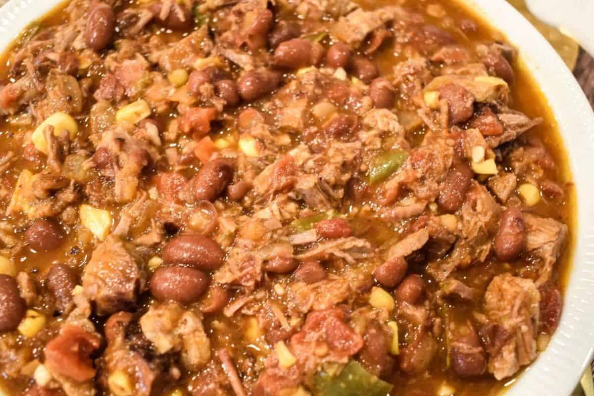 A close-up of a bowl filled with must try chili—packed with shredded meat, red beans, corn, tomatoes, and green peppers in a thick sauce.