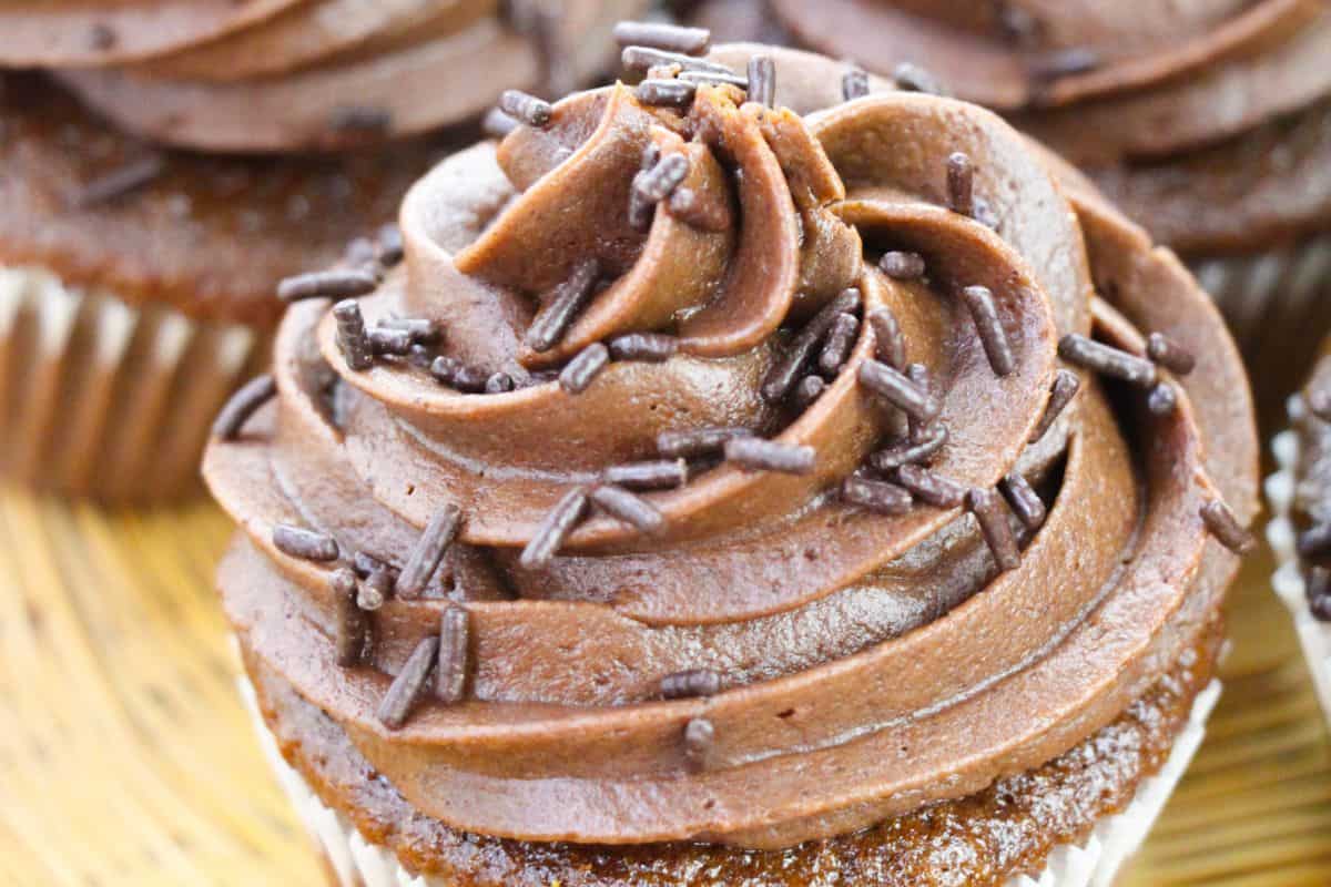 Close-up of a chocolate cupcake with swirled chocolate frosting and chocolate sprinkles on top, perfect for making party moments sweeter.