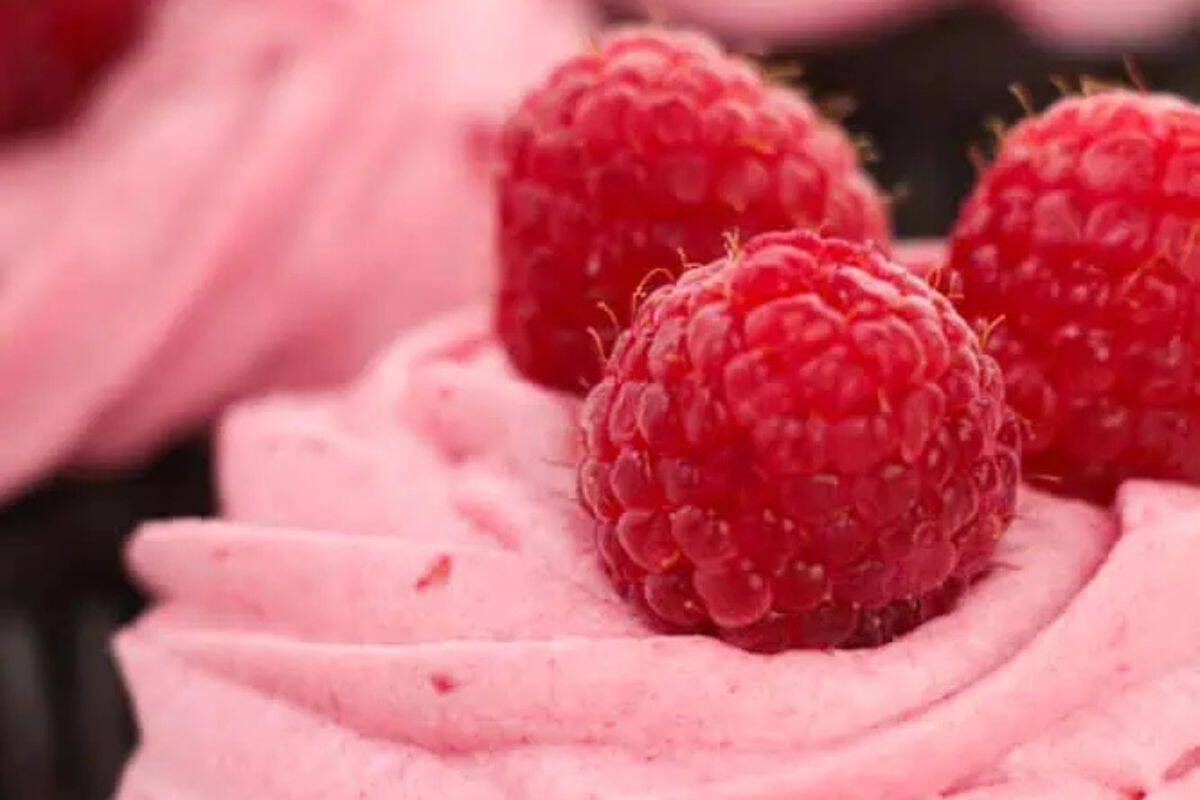 A close-up of a delightful dessert showcases pink frosting crowned with two fresh raspberries, making it a sweeter choice for any party. Perfect for those exploring new cupcake recipes!.