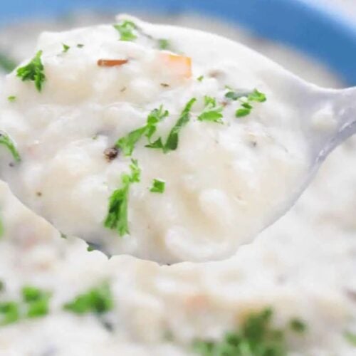 A close-up of a spoonful of creamy rice soup garnished with chopped parsley, held over a bowl of the same soup—a perfect choice for fans of quick soups and comforting soups.
