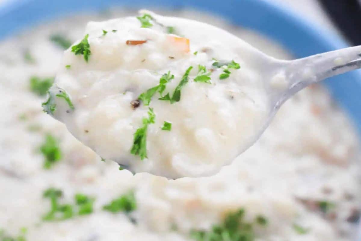 A close-up of a spoonful of creamy rice soup garnished with chopped parsley, held over a bowl of the same soup—a perfect choice for fans of quick soups and comforting soups.