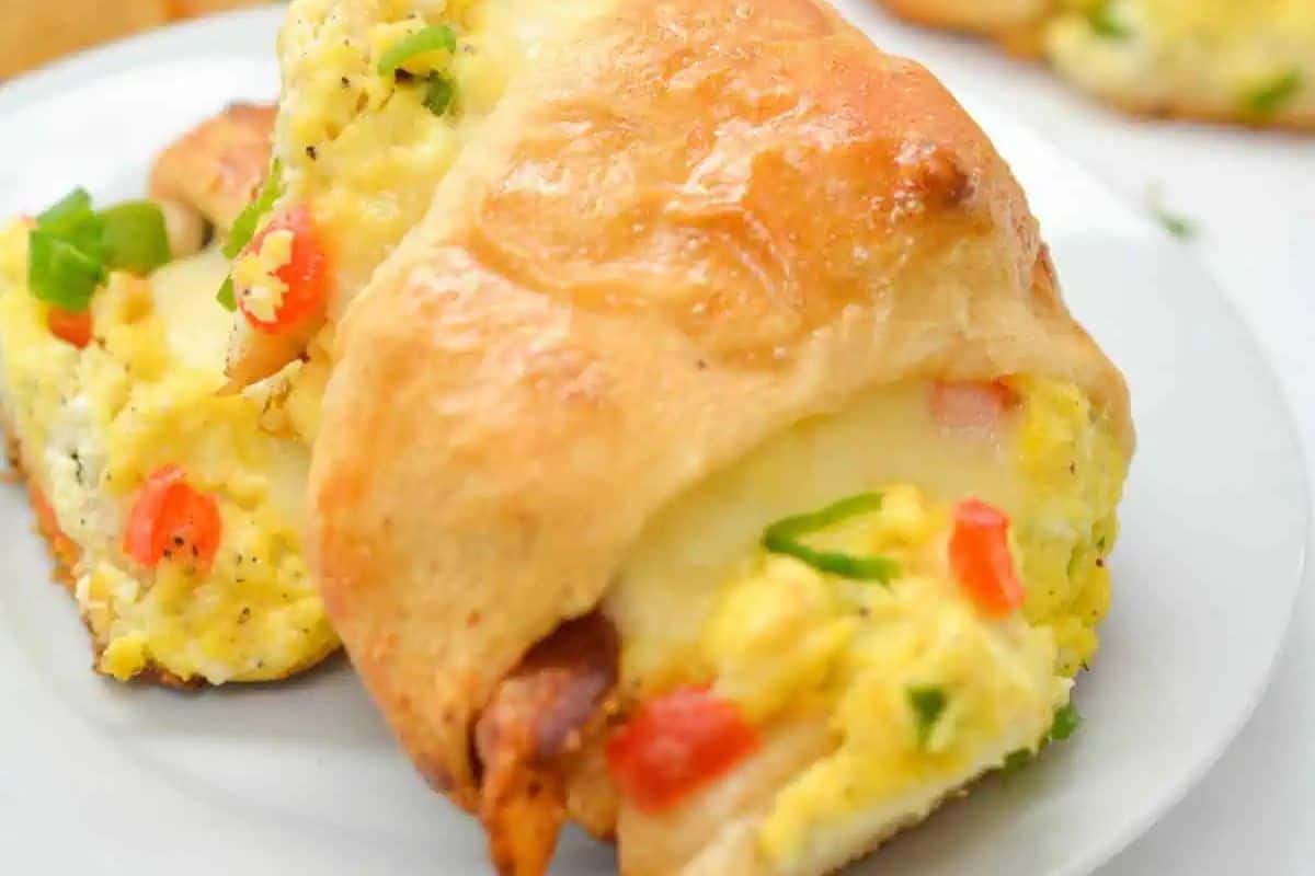A sweet and savory breakfast croissant stuffed with scrambled eggs, cheese, bacon, and diced red and green peppers on a white plate—perfect for brunch recipes or a special Valentine's Day breakfast.