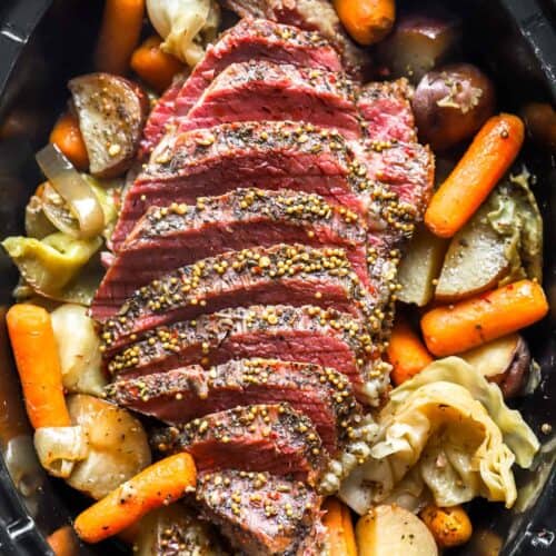 Sliced corned beef with mustard seeds nestled atop potatoes, carrots, and cabbage in a slow cooker makes for an Irish-inspired dinner perfect for St. Patrick's Day celebrations.