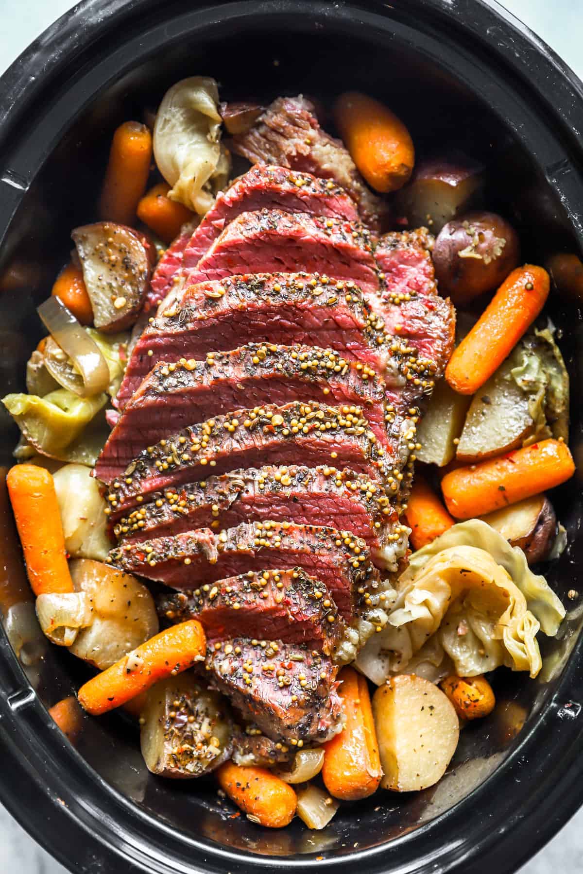 Sliced corned beef with mustard seeds nestled atop potatoes, carrots, and cabbage in a slow cooker makes for an Irish-inspired dinner perfect for St. Patrick's Day celebrations.