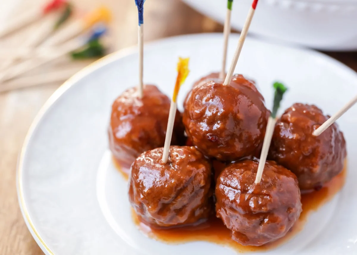 Five sauce-covered meatballs sit invitingly on a white plate, each with a toothpick on top, making them perfect potluck dishes. These foolproof recipes will have everyone recipe asking at your next gathering.