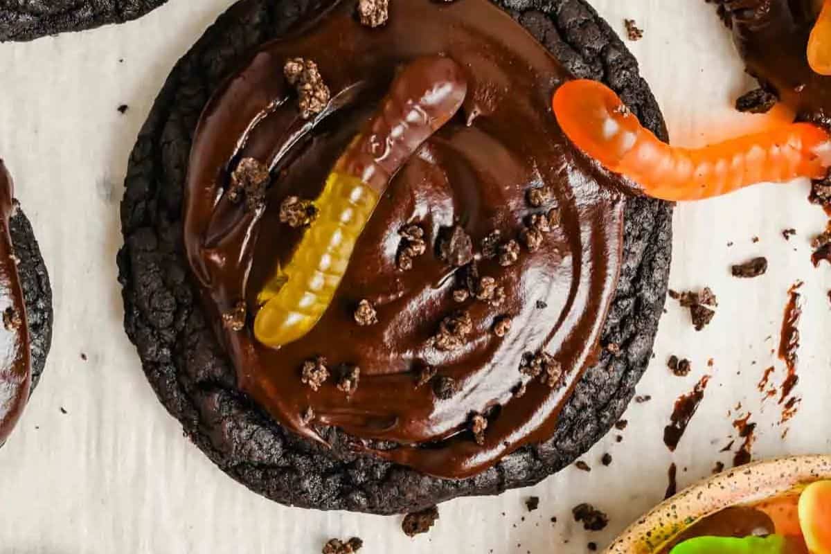 A chocolate cookie topped with chocolate frosting, chocolate crumbs, and gummy worms—these creative bake sale treats are sure to wow your crowd on any light-colored display.