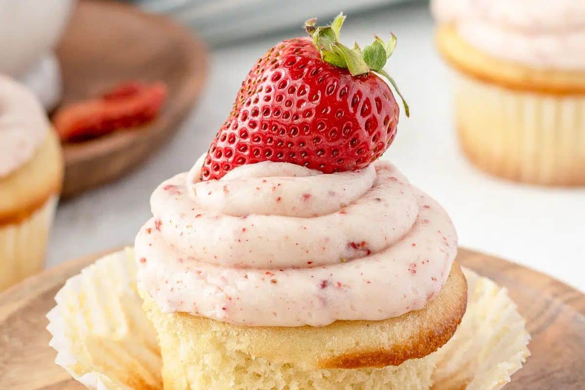 Discover the sweeter side of party treats with a vanilla cupcake adorned in strawberry frosting, crowned by a fresh strawberry atop an unwrapped cupcake liner.