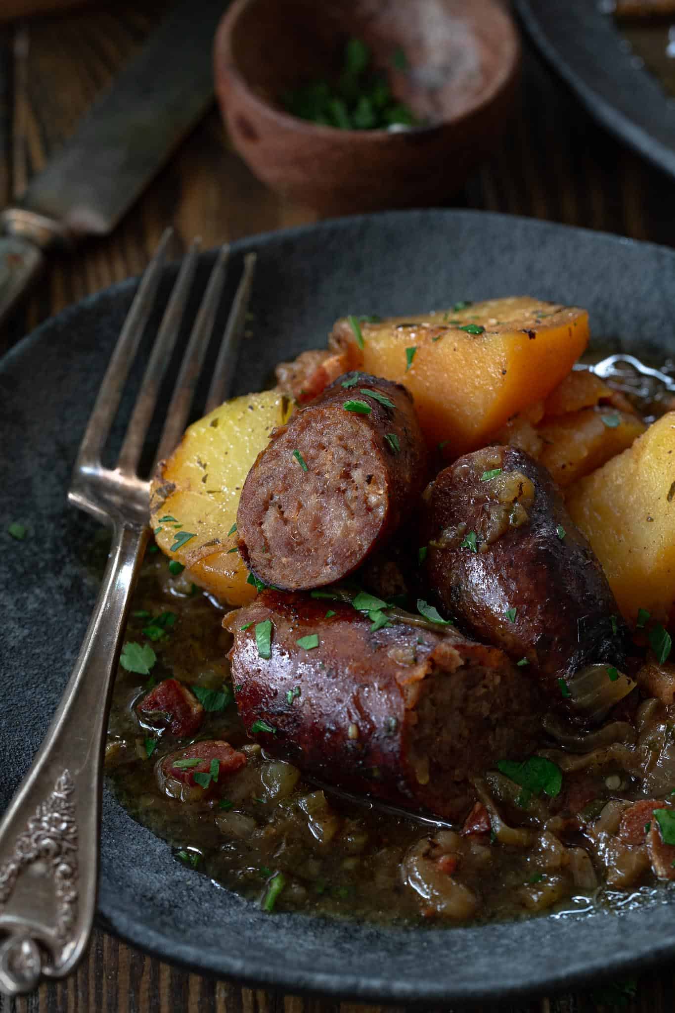 A plate with sliced sausage, potatoes, and herbs, perfect for Irish-inspired dinners or St. Patrick’s Day celebrations, served with a fork on a dark ceramic dish.