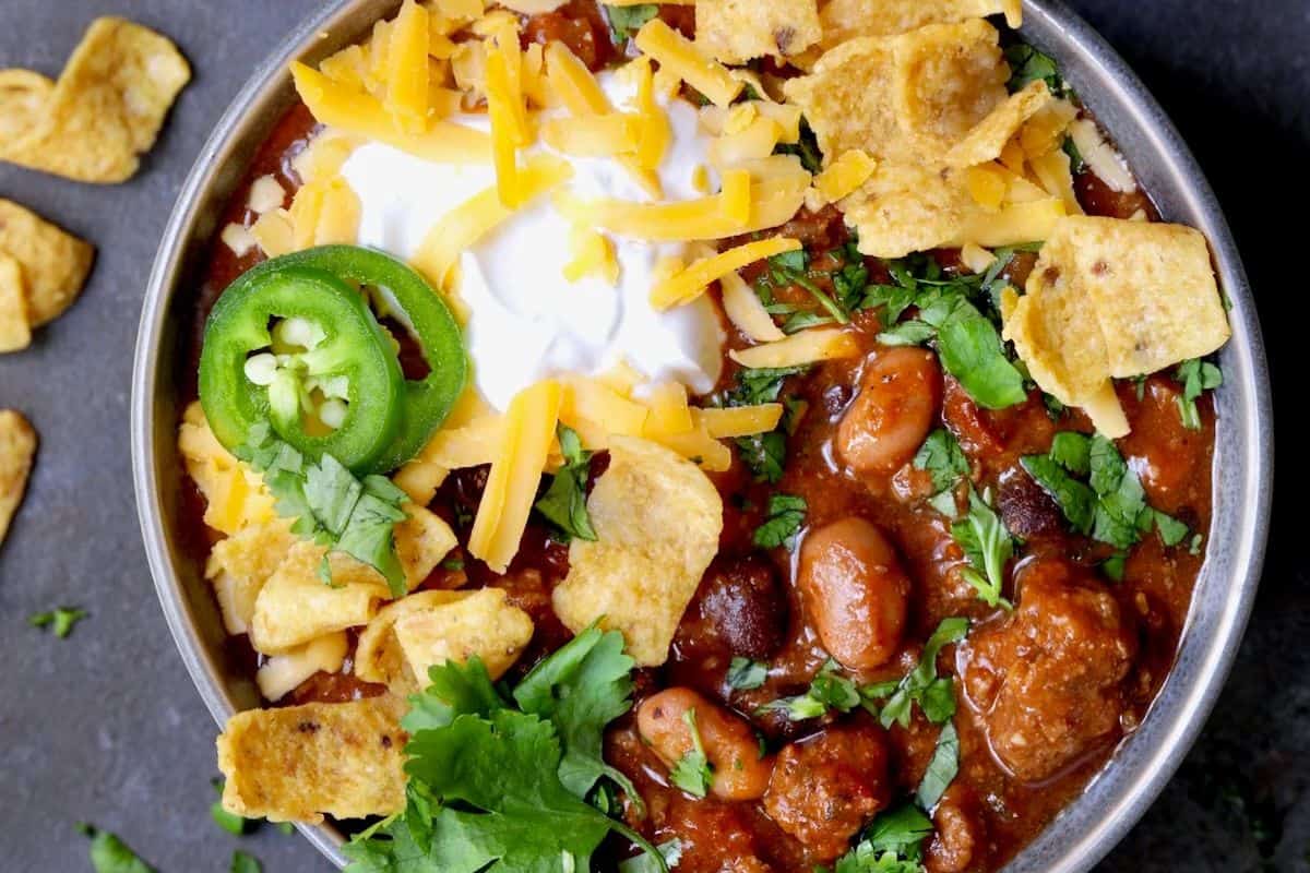 A must-try bowl of chili topped with shredded cheddar cheese, sour cream, sliced jalapeño, corn chips, and chopped cilantro—a classic everyone loves. Perfect for fans of hearty chili recipes!.