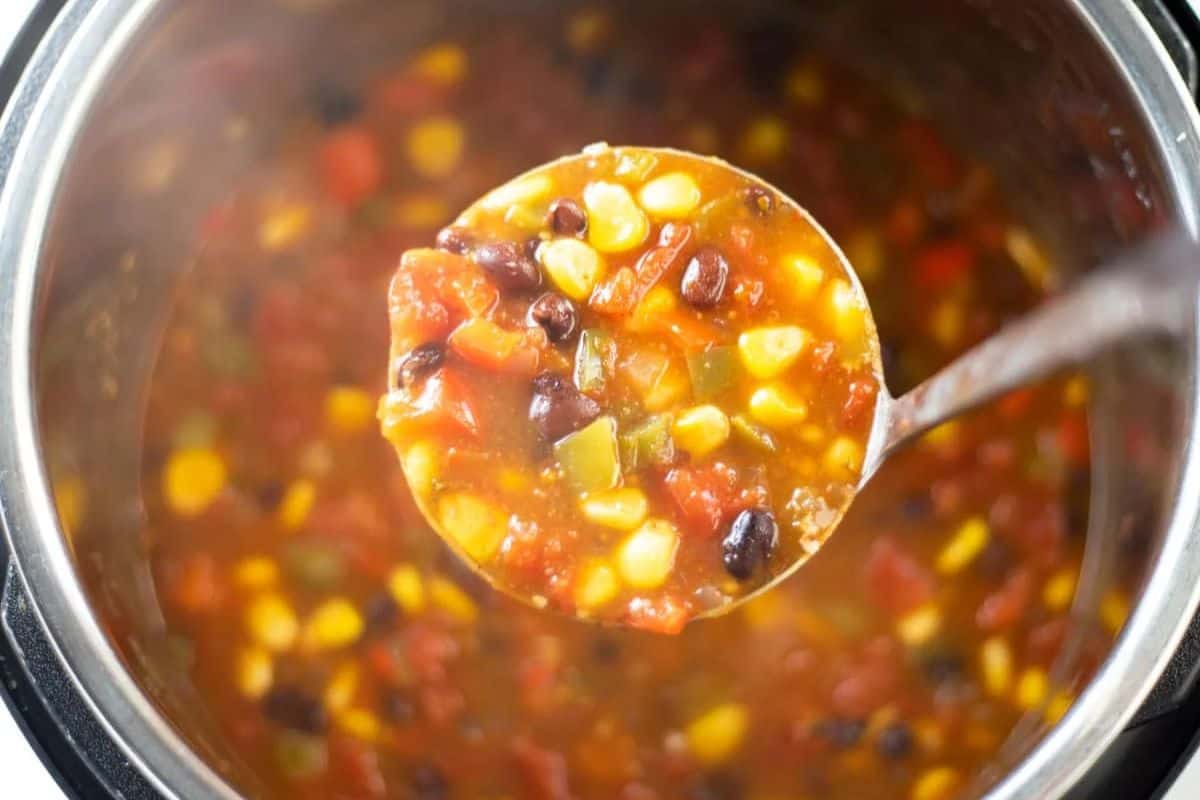 A ladle holding tomato-based soup with black beans, corn, peppers, and tomatoes over a pot of the same soup—perfect for fans of comforting soups and quick soup recipes.