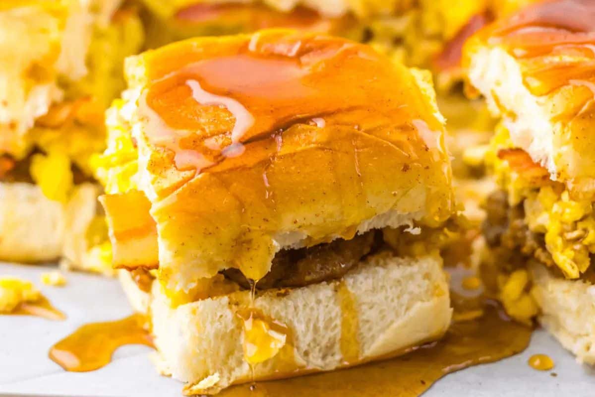 A sweet and savory breakfast slider with scrambled eggs, sausage, and melted cheese on a soft bun topped with syrup—perfect for brunch recipes or a special Valentine's Day breakfast.