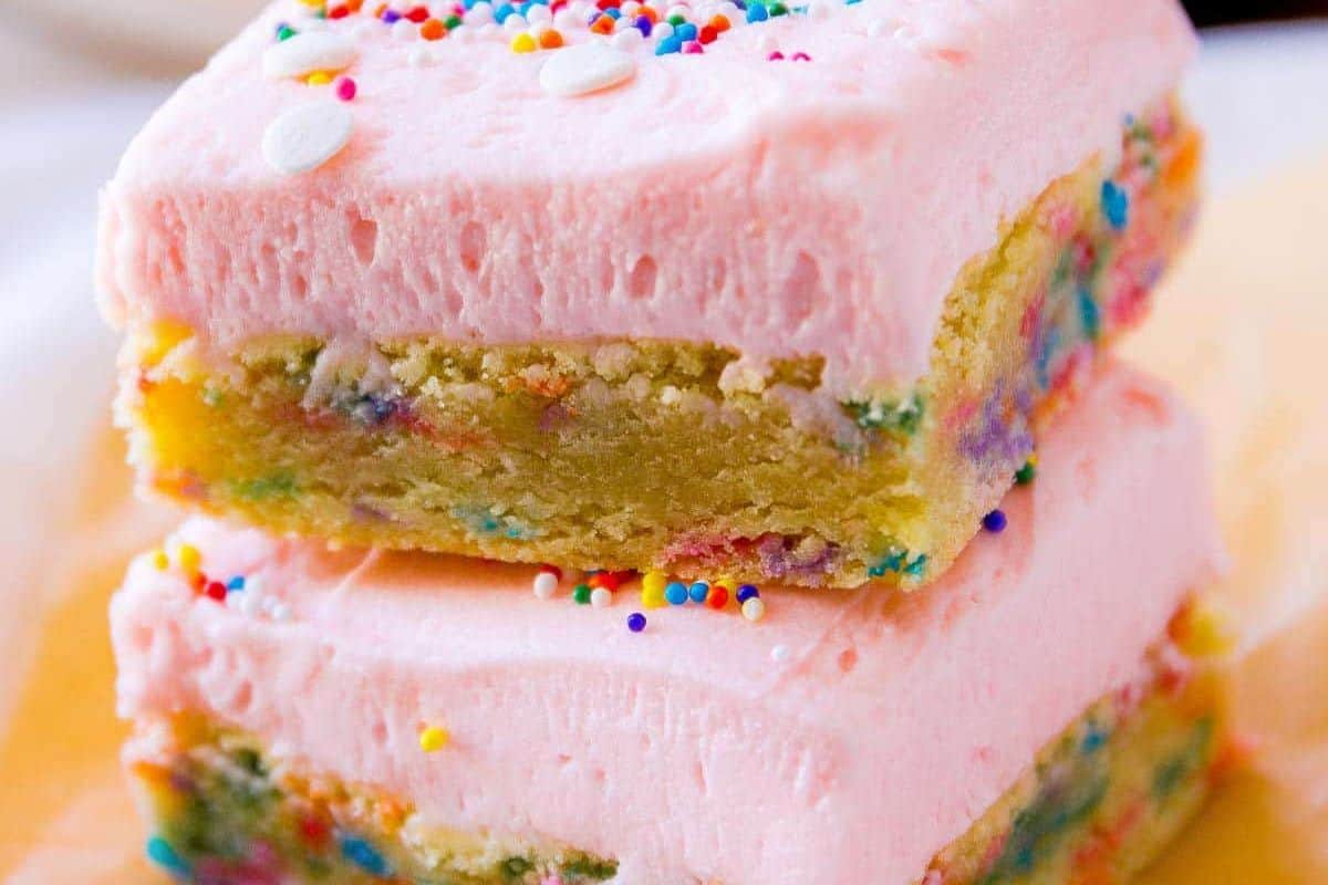 Two square cookie bars with pink frosting and colorful sprinkles are stacked on top of each other, making them perfect bake sale treats and sure to be crowd-pleasing desserts.