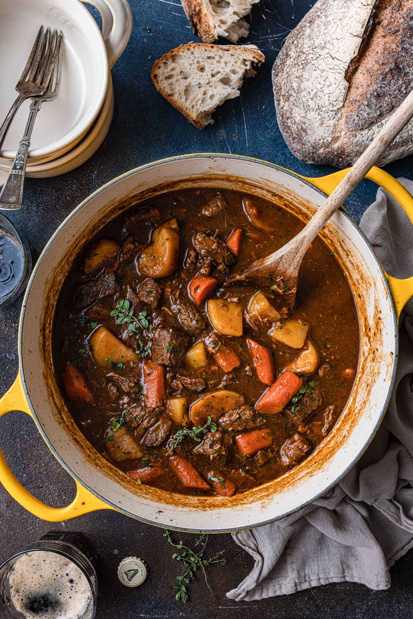 A pot of beef stew with carrots and potatoes, perfect for Irish-inspired dinners, accompanied by slices of bread on a dark surface.