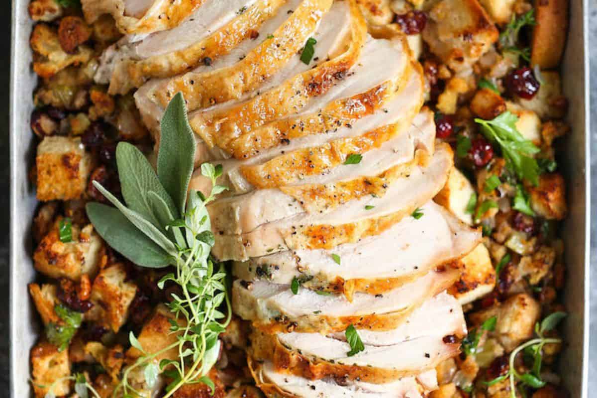 Sliced roasted turkey breast served on a bed of bread stuffing with herbs and cranberries, garnished with fresh sage and thyme—a perfect sheet pan meal for easy cleanup and delicious meals every time.