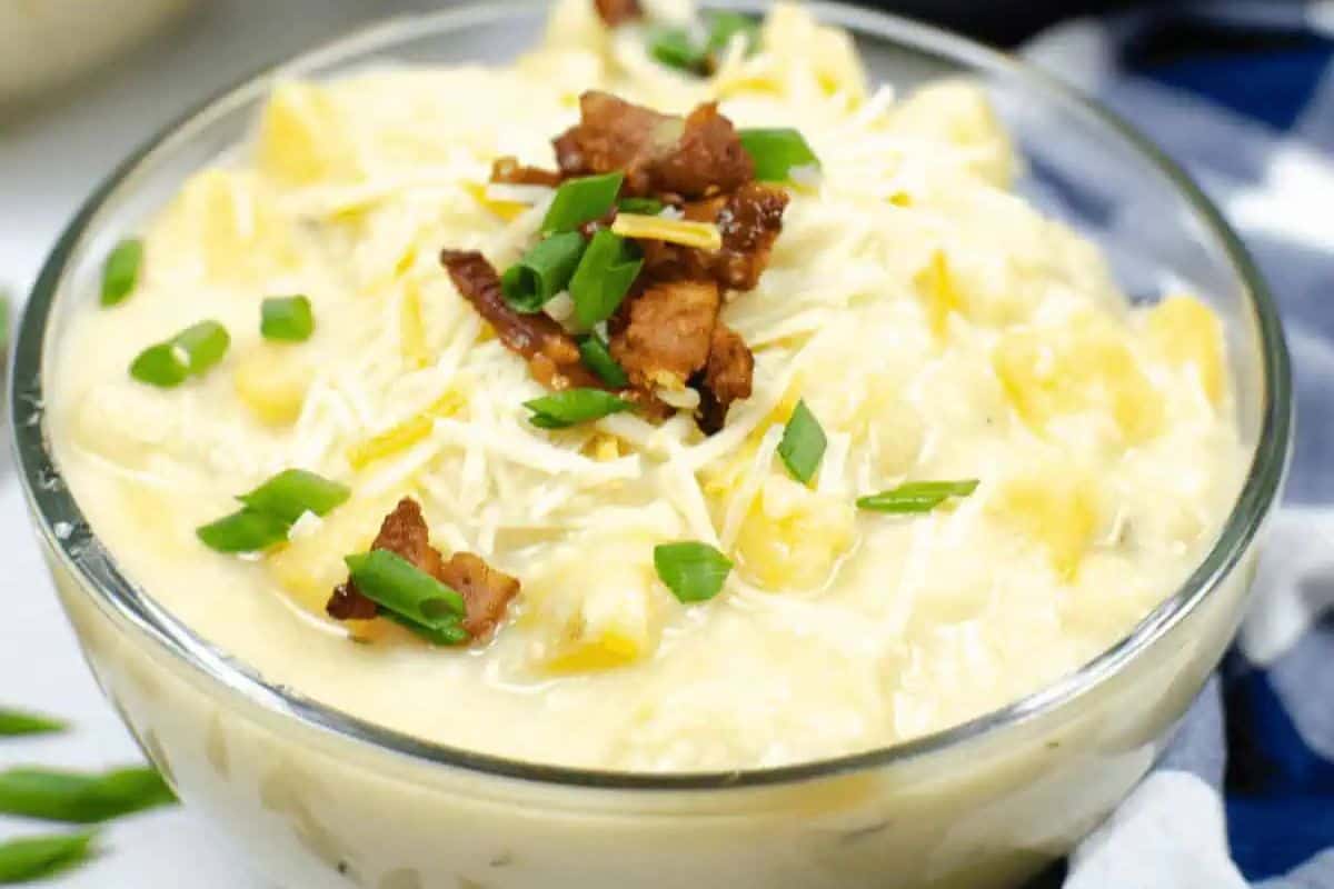 A bowl of creamy potato soup topped with shredded cheese, crispy bacon pieces, and chopped green onions—perfect for fans of quick soup recipes and comforting soups.