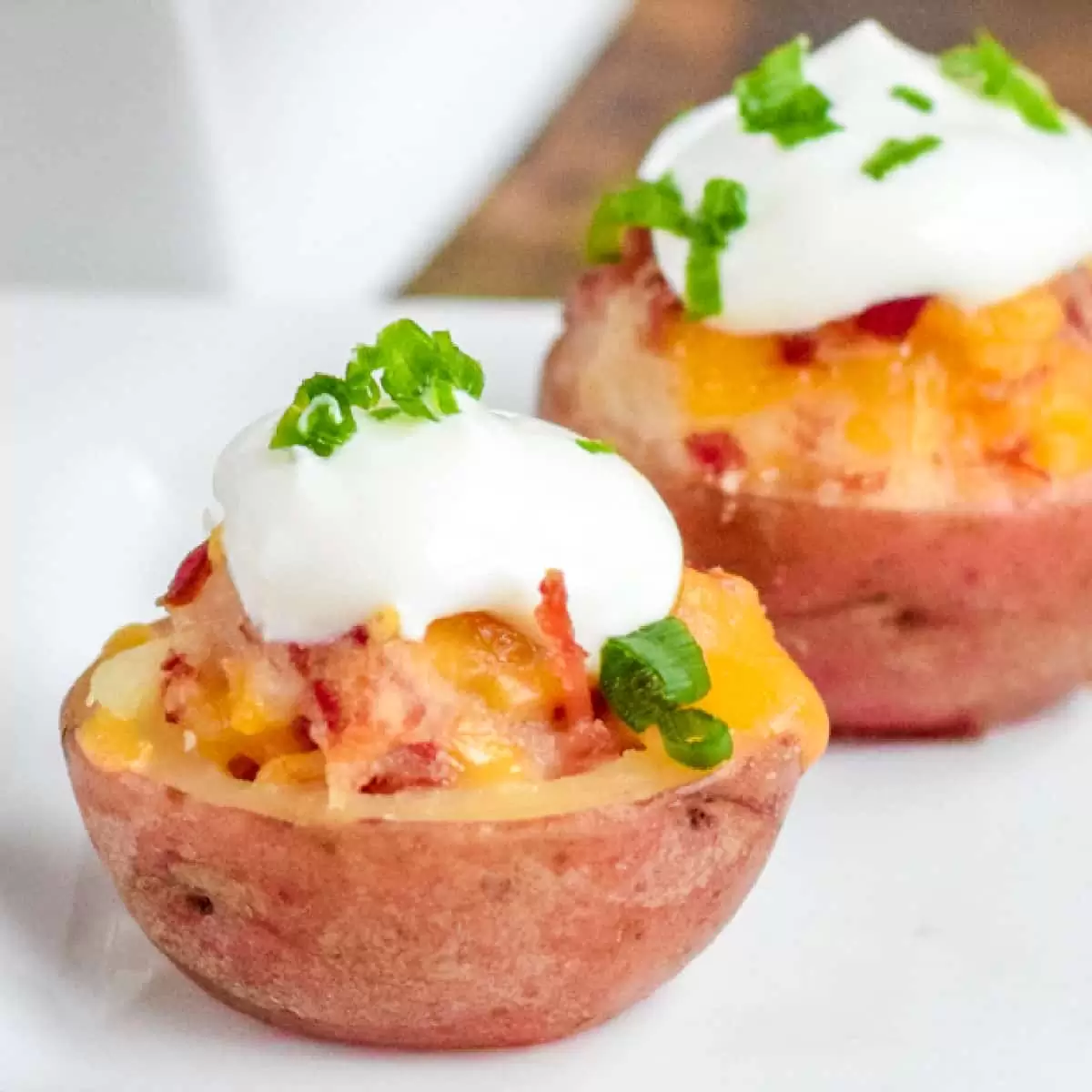 Two halved potatoes topped with melted cheese, bacon bits, sour cream, and chopped green onions on a white plate—a perfect treat for St. Patrick’s Day celebrations.