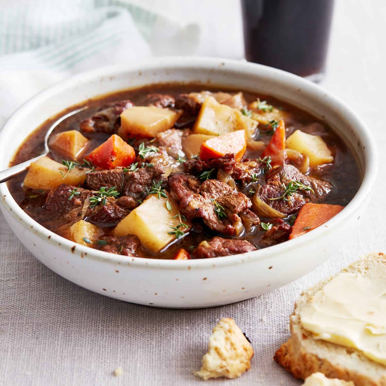 A bowl of beef stew with chunks of beef, potatoes, and carrots, garnished with herbs, perfect for Irish-inspired dinners. A piece of buttered bread sits on the side, making it an ideal dish for St. Patrick’s Day celebrations.