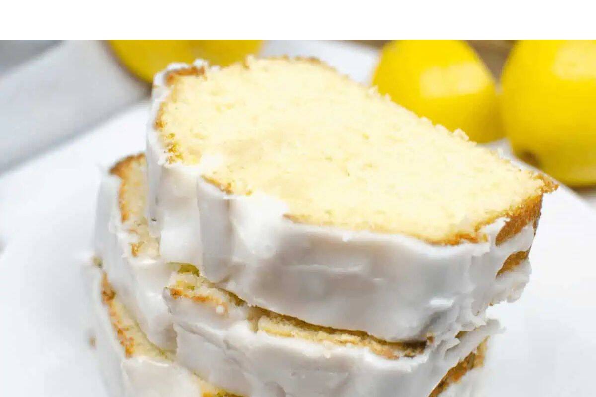 Two slices of lemon pound cake with white icing are stacked on a white plate, with whole lemons in the background—perfect crowd-pleasing desserts for your next creative bake sale.