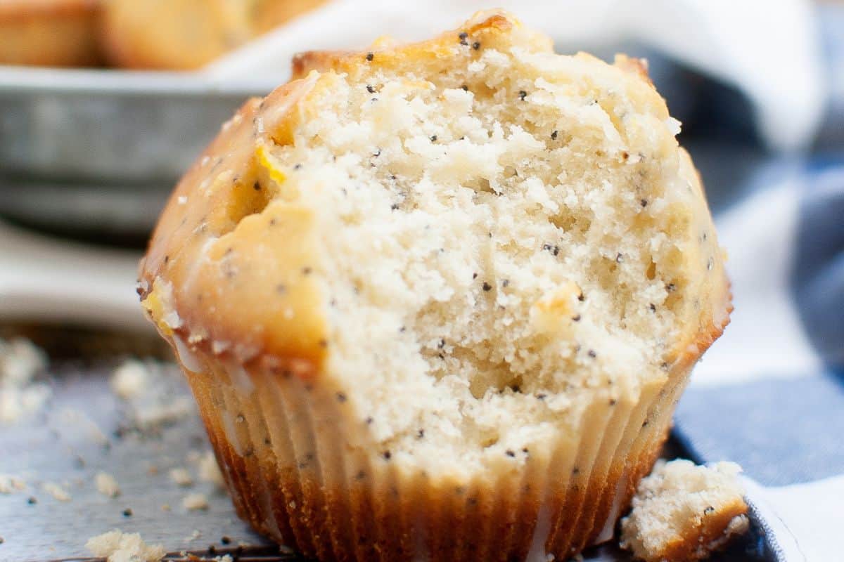 A lemon poppy seed muffin with a bite taken out, showing its moist texture. Crumbs are scattered around like confetti at a party.