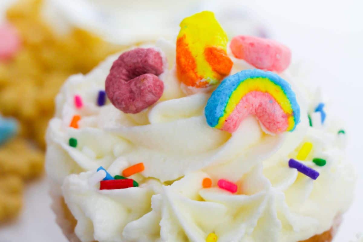 This party-ready cupcake features white frosting adorned with colorful cereal pieces and rainbow sprinkles, perfect for those who crave sweeter delights.