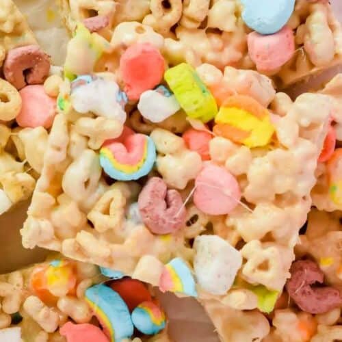 Close-up of cereal bars made with colorful marshmallows and cereal pieces, cut into squares and stacked on a white surface—perfect bake sale treats to wow your crowd with their fun colors and tasty crunch.