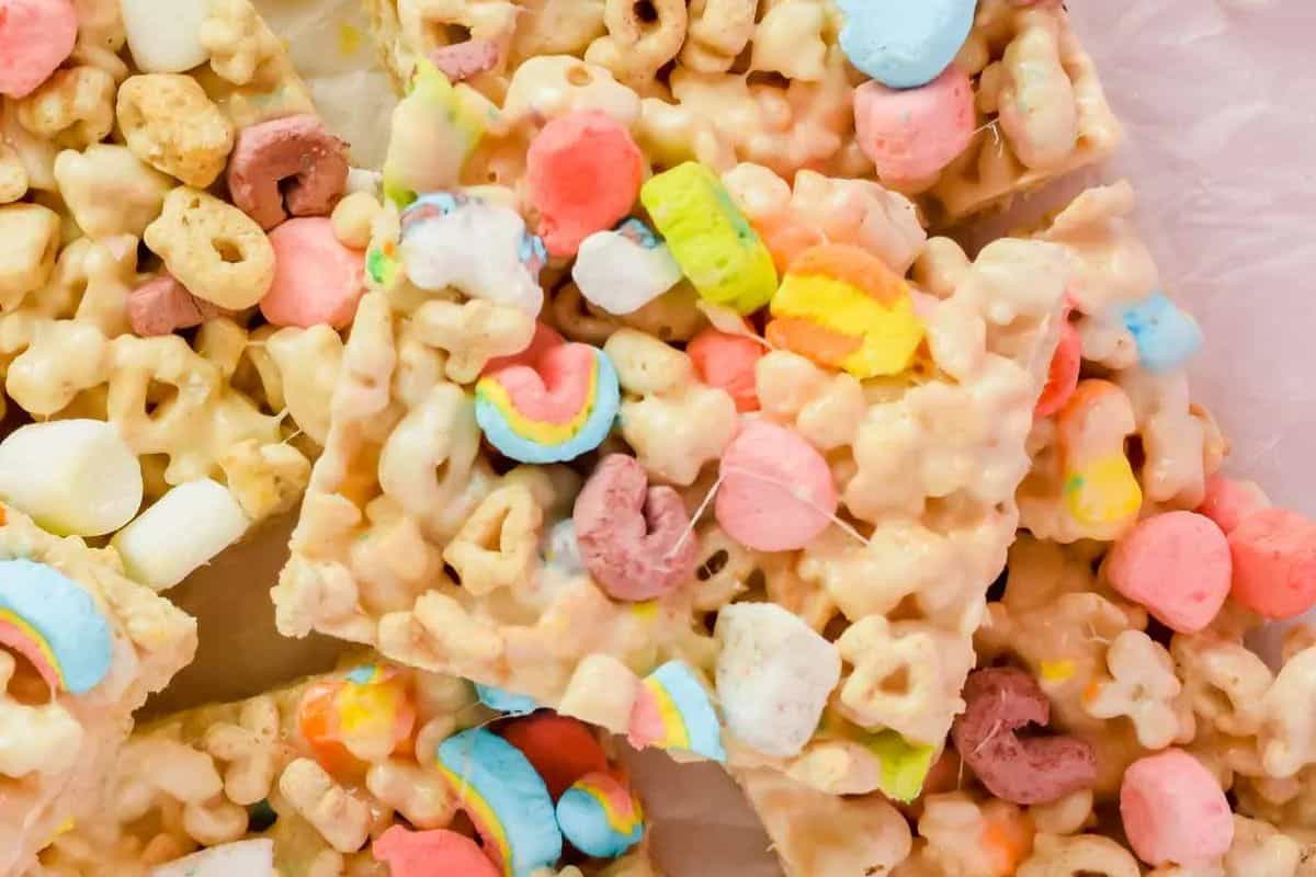 Close-up of cereal bars made with colorful marshmallows and cereal pieces, cut into squares and stacked on a white surface—perfect bake sale treats to wow your crowd with their fun colors and tasty crunch.