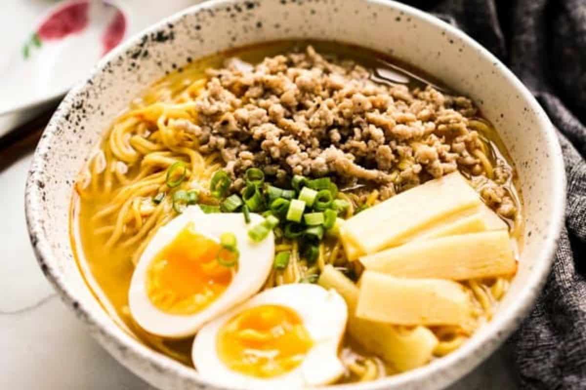 A bowl of ramen with sliced soft-boiled eggs, ground meat, bamboo shoots, chopped green onions, and noodles in broth—perfect for those craving comforting soups or quick soups ready in under 30 minutes.