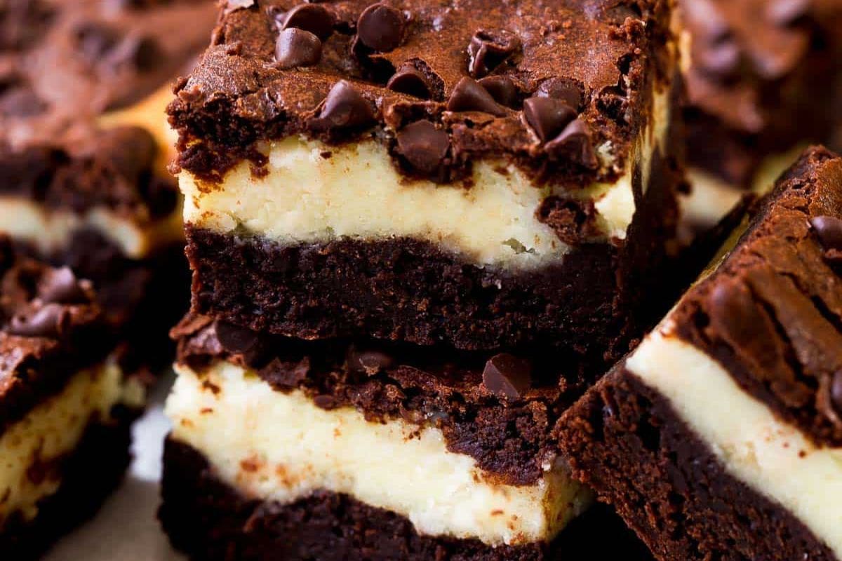 Stacked chocolate brownies with a creamy cheesecake layer in the middle and chocolate chips on top—these crowd-pleasing desserts are perfect for your next creative bake sale.