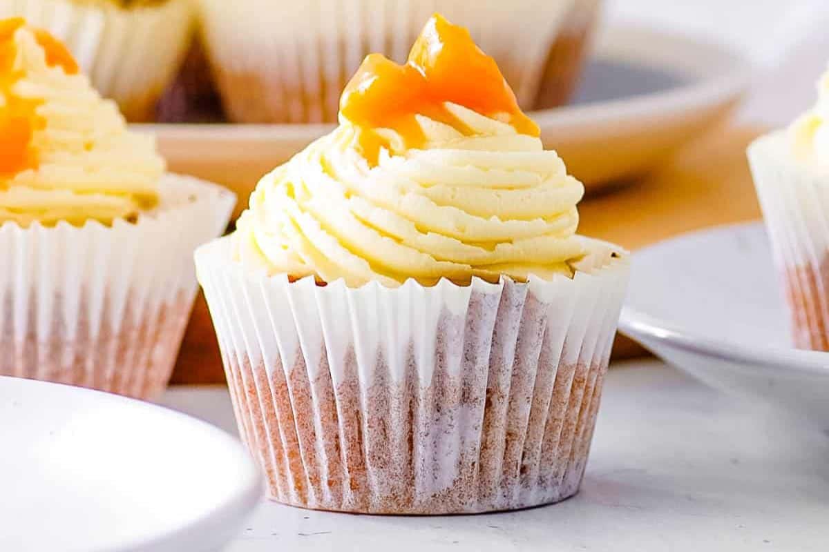 Sweeter cupcake with cream-colored frosting artfully swirled on top, garnished with small orange pieces. Nestled in a white paper liner and placed on a white surface, it's perfect for party gatherings or trying your hand at new cupcake recipes.