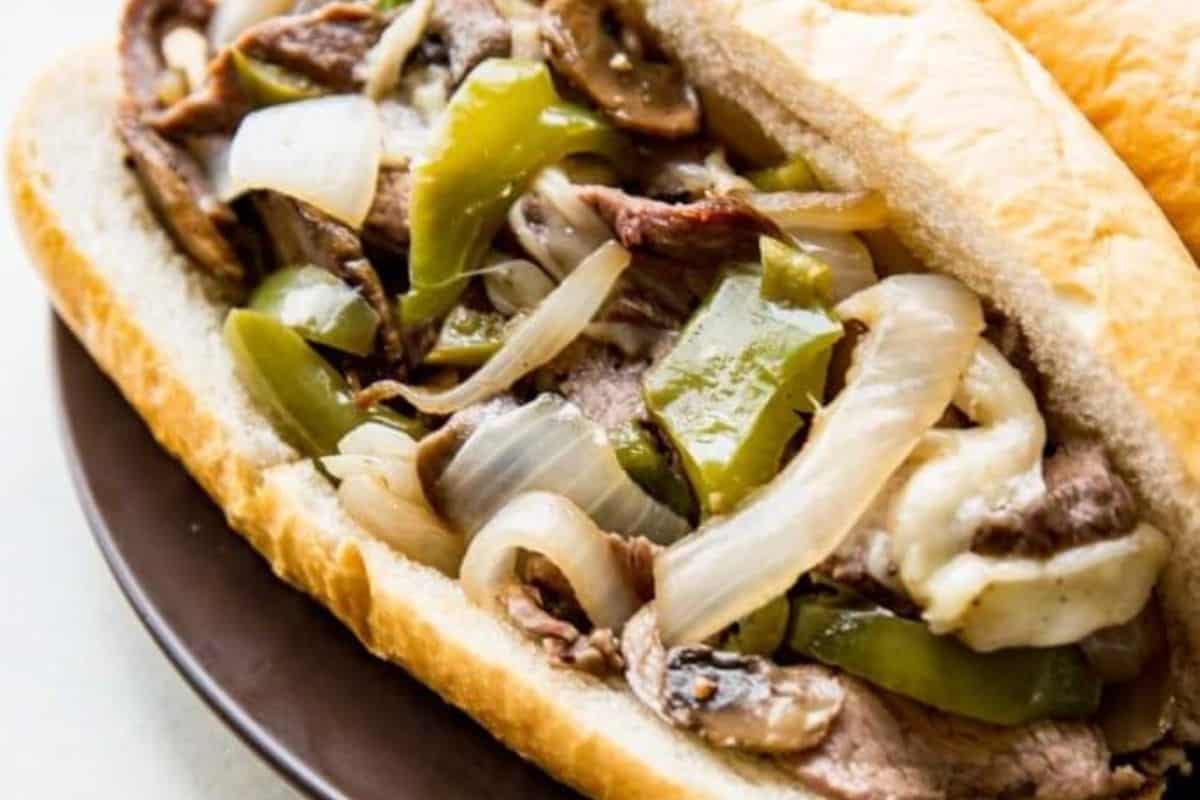 A close-up of a sandwich filled with sliced beef, sautéed green peppers, onions, mushrooms, and melted cheese on a hoagie roll—one of the most delicious meals for any sheet pan meals fan.
