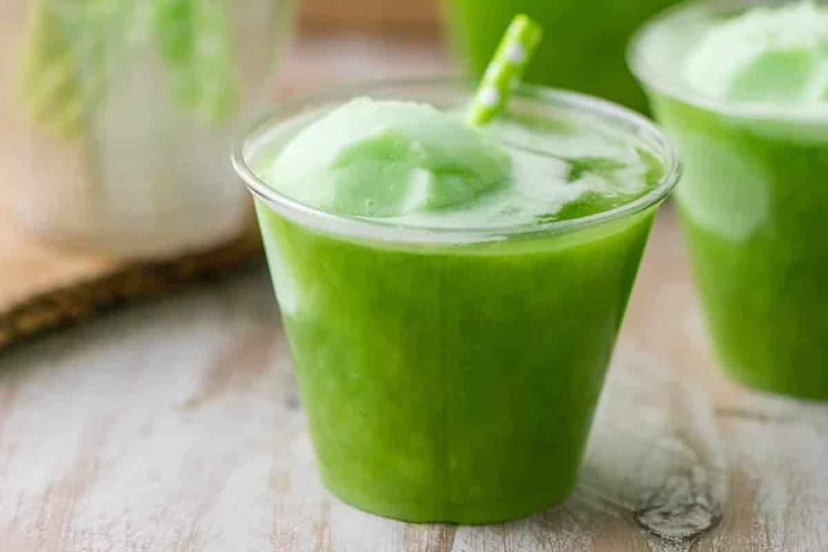 A vibrant green slushy drink in a clear plastic cup with a green straw sits on a wooden surface, perfectly capturing the Irish spirit of St. Patrick's Day.